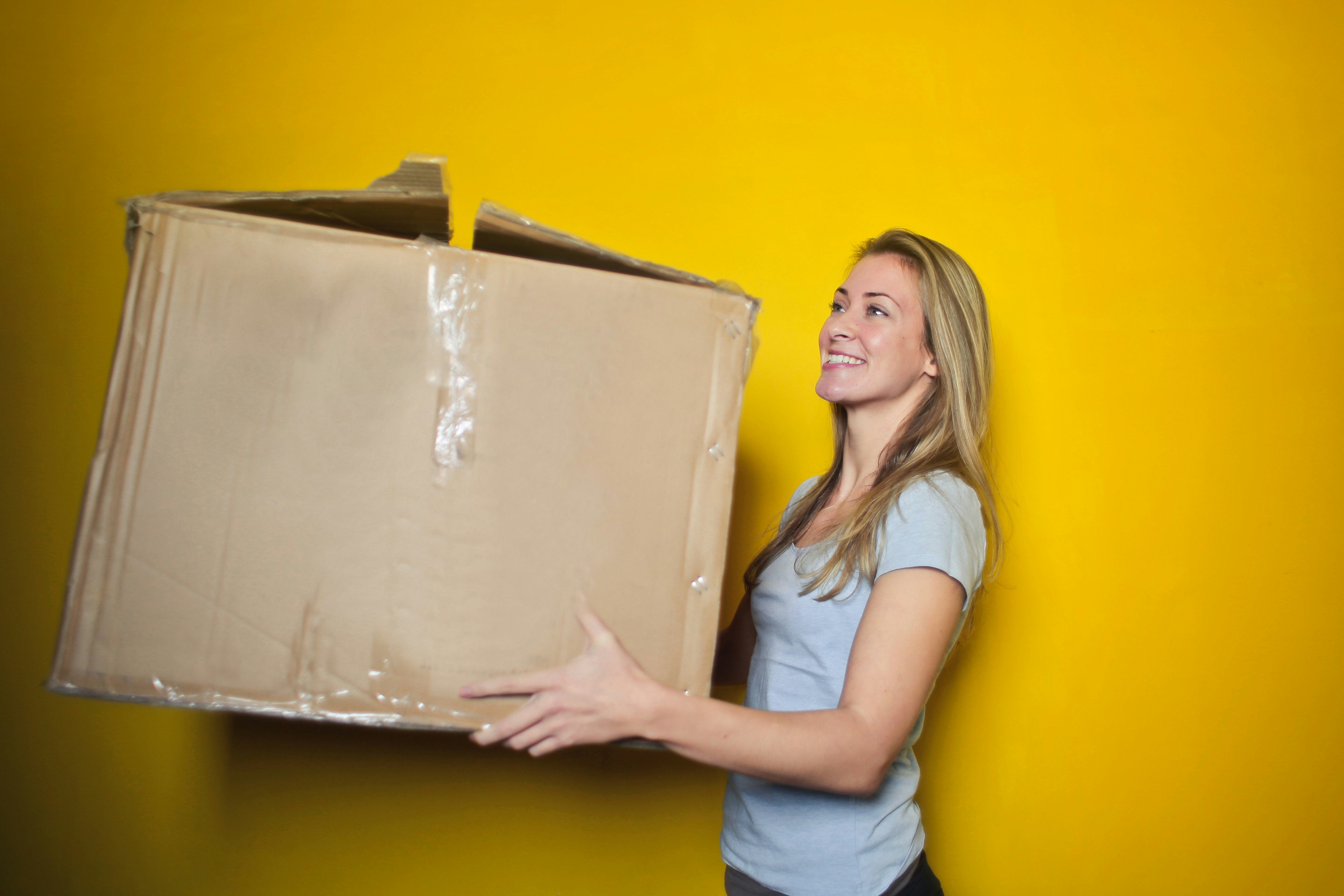 A happy blonde woman carrying a moving box